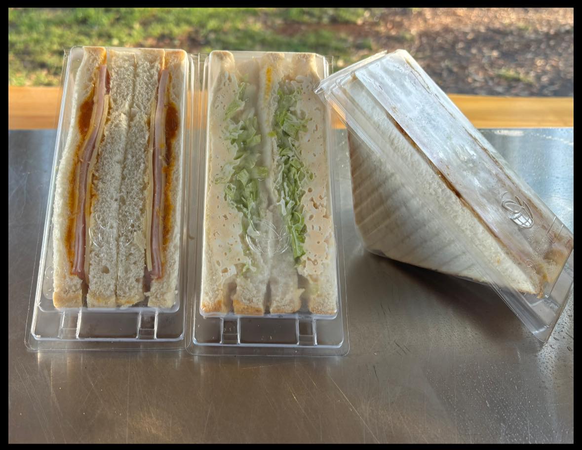 Fresh ham, cheese and salad sandwiches in clear takeaway packs on a stainless bench