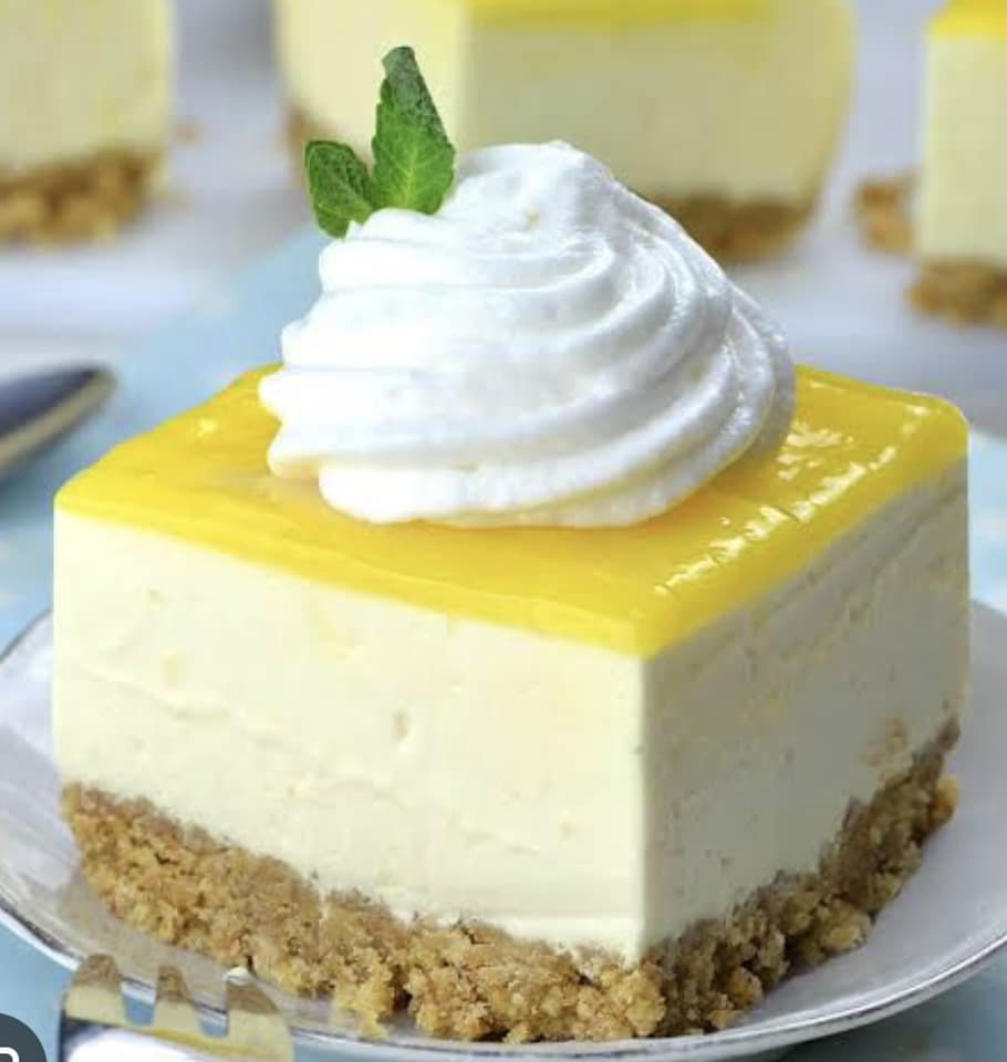 Lemon cheesecake slice topped with whipped cream, lemon curd and a mint leaf