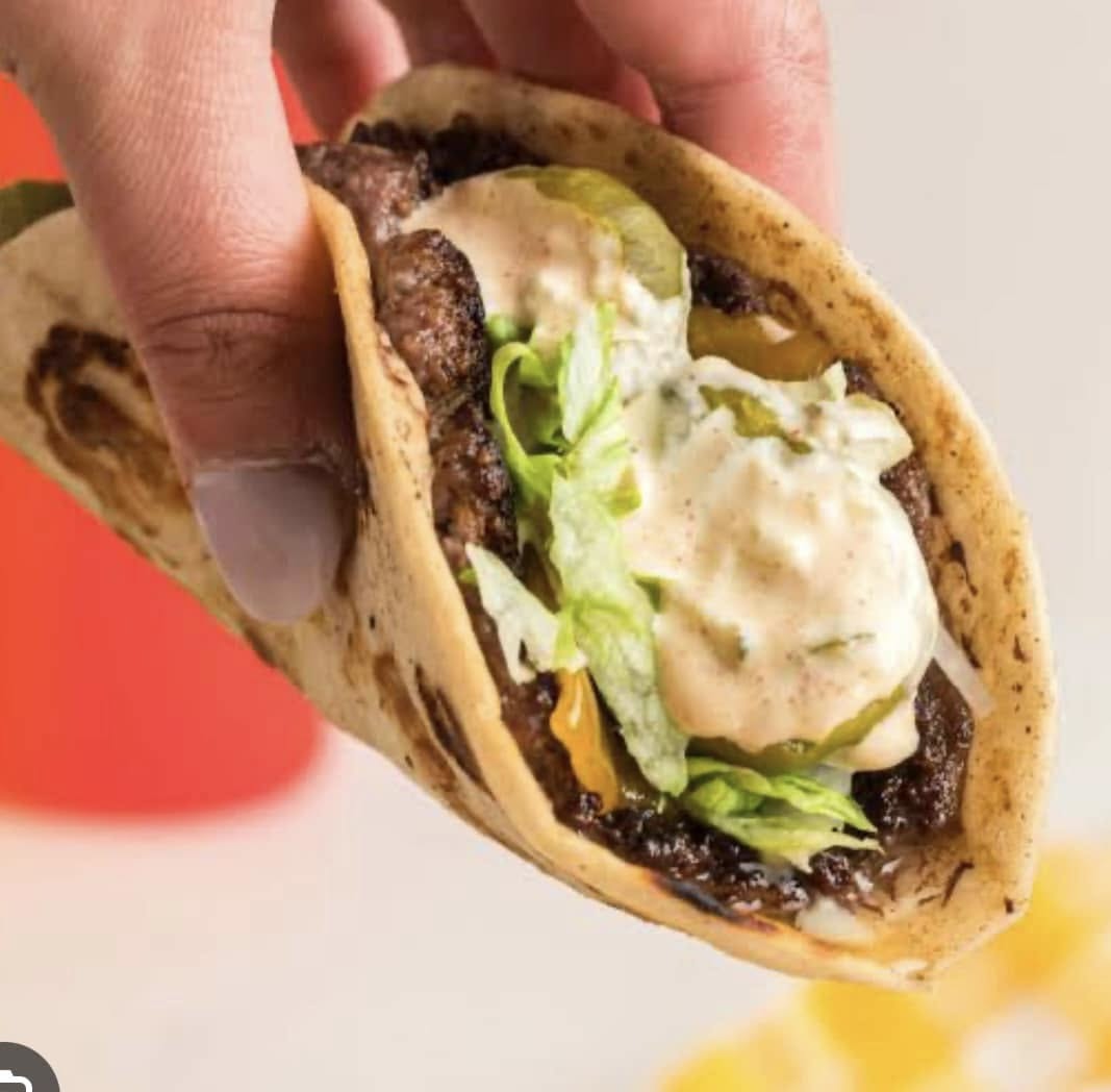 Hand holding a gourmet beef taco with lettuce, pickles and creamy chipotle sauce